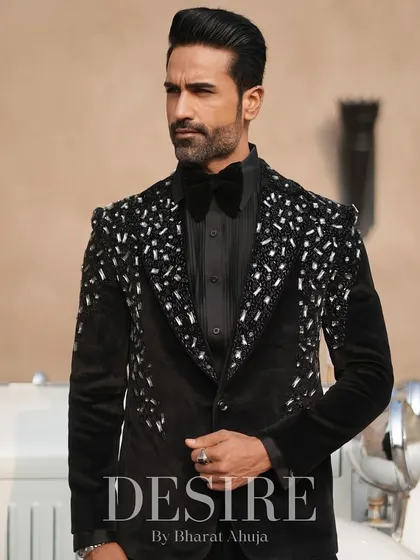 A powerful stance in the black velvet tuxedo with silver scatter embroidery. The vintage car in the background complements the timeless elegance of the suit.