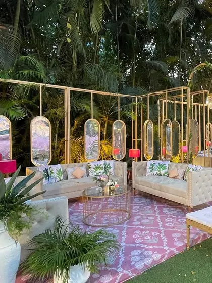 A chic lounge area at the Mamera event, with modern gold-framed structures, hanging mirrors, and comfortable sofas set on a pink patterned rug.