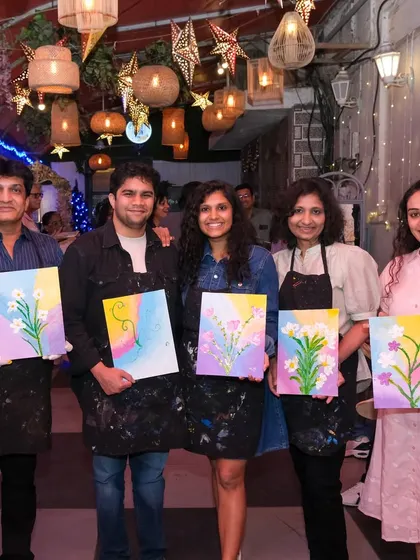 A group of friends and family proudly hold their floral paintings at a private art party, showing how art can be a wonderful way to celebrate together.