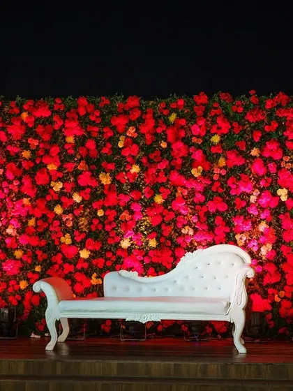A vibrant floral photo booth for a rooftop wedding. The dense wall of red and yellow flowers against the night sky provides a dramatic and beautiful spot for guests to capture memories.
