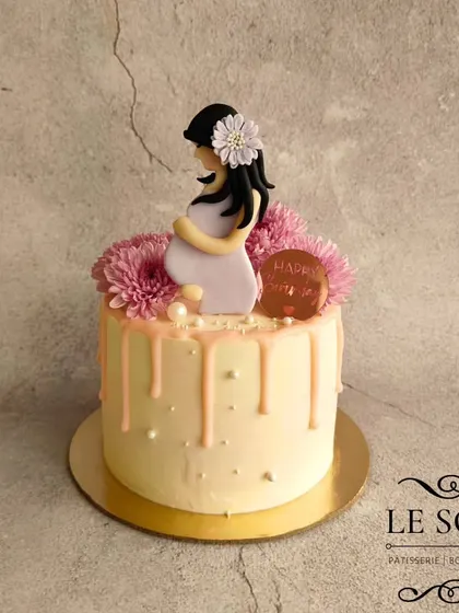 A beautiful cake for a mom-to-be, made by a new mom. This half-kg Vanilla Butterscotch cake has a soft pink drip, fresh flowers, and a serene fondant figurine of an expecting mother.