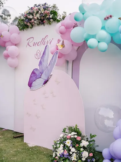 This outdoor butterfly-themed setup uses large printed panels with butterfly graphics, complemented by fresh flowers and pastel balloon clusters for an elegant and modern look.