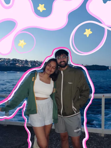 A cute couple photo by the sea, outlined in pink and surrounded by dreamy clouds and stars.