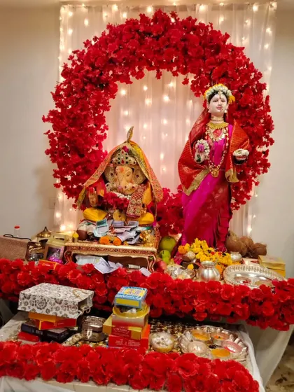 This Gauri Ganpati setup features a bold circular arch of red flowers against a white curtain with fairy lights. The all-red theme creates a striking and powerful festive statement.