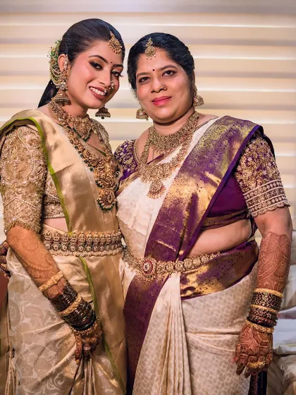 A beautiful moment between the bride and her mother. Both are wearing custom-designed blouses that complement their sarees, with the bride in a stunning gold and the mother in a classic white and purple.