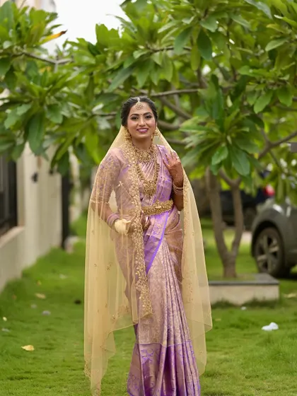 A full-length view of the bride's stunning lavender ensemble. The makeup is designed to complement the rich color of the saree and the intricate gold jewellery.