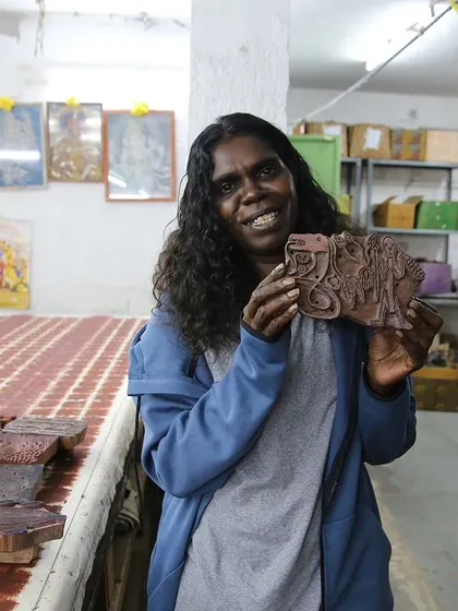 An artist from the Bábbarra Women's Centre proudly holds a woodblock carved from her design. This project is about translating ancestral stories from one medium (lino) to another (wood).