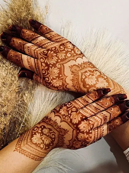 A gorgeous full-hand design for Eid, featuring intricate floral and paisley patterns. The dark stain on the fingertips is a traditional touch that enhances the beauty of the design.