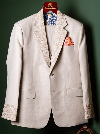 Craftsmanship is visible in the details. This bespoke linen jacket features intricate, hand-guided embroidery on the lapels and cuffs, paired with a vibrant silk pocket square. It is a testament to our dedication to creating garments that are unique and timeless.