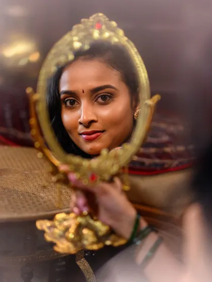 A 'Kanmani' moment. This conceptual shot uses a mirror to create a story of self-reflection and femininity. The soft, dreamy lighting and traditional setting add to the poetic feel of the portrait.