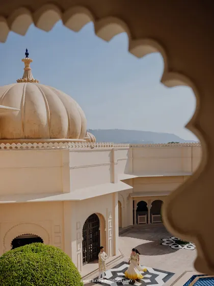 A view through a scalloped archway captures the couple walking across a courtyard at Udaivilas during their Haldi ceremony.
