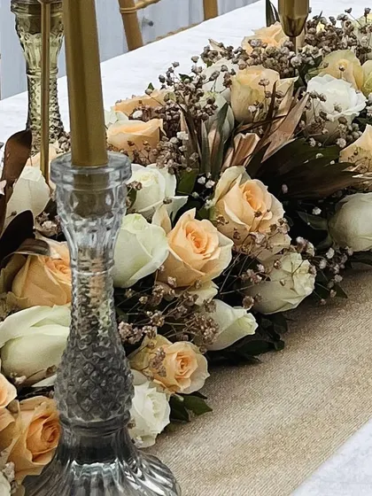An elegant tablescape featuring a long floral runner of peach and white roses, baby's breath, and tall glass candle holders.
