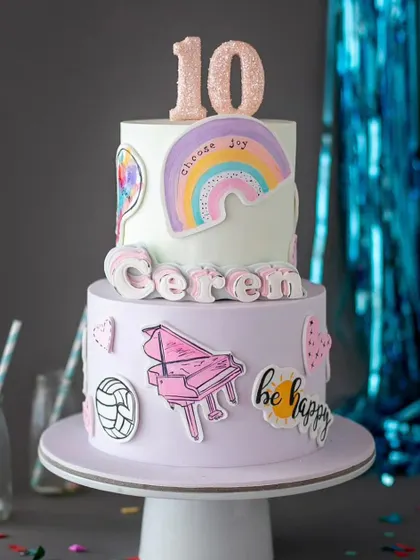 A cool and trendy cake for a 10th birthday. This two-tiered cake is decorated with fun patches like a piano, a rainbow, and "be happy" messages.