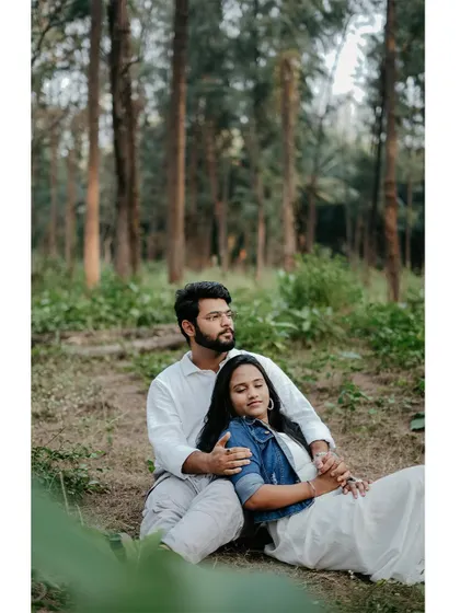 A peaceful moment with a couple relaxing in a forest. She is resting in his lap as they both look content, capturing a quiet and intimate connection.