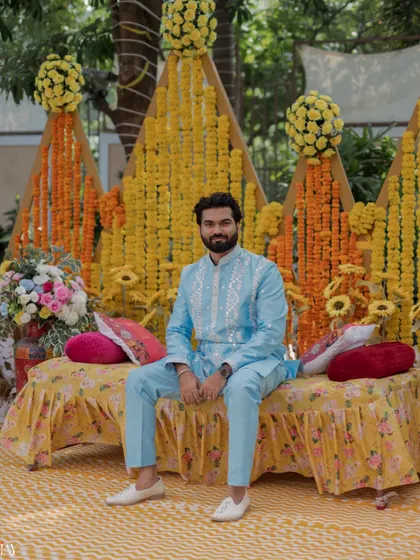 A portrait of the groom seated against the vibrant marigold decor of the Haldi ceremony.