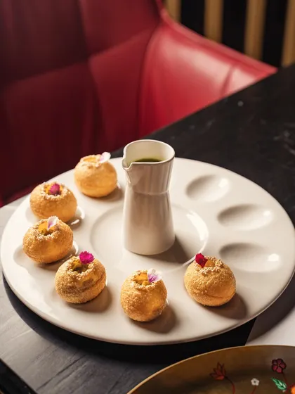 An elegant presentation of pani puri on a specialized ceramic plate. The moody lighting and clean composition highlight the dish as a piece of culinary art.