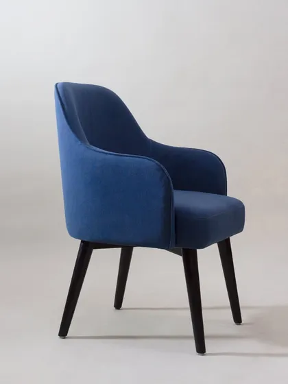 The side profile of the blue armchair shows its elegant silhouette and sturdy wooden legs.