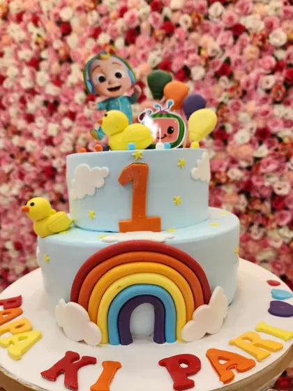 This two-tiered Cocomelon cake is perfect for a first birthday. It features a bright rainbow, fluffy clouds, and the beloved characters, creating a cheerful and colorful design.