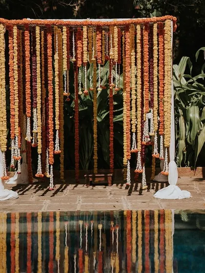 A beautiful backdrop of hanging marigold garlands in shades of orange and yellow, creating a warm and traditional setting by the pool.