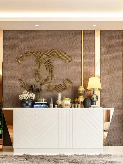 A luxurious foyer console in white with a chevron pattern. The backdrop features textured wallpaper, wood paneling, and a large metallic logo, creating a high-fashion, branded look.