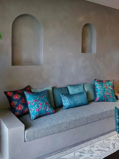 A built-in sofa against a grey lime-washed wall with arched niches. The space is brought to life with vibrant teal and floral cushions, adding a pop of color and personality.