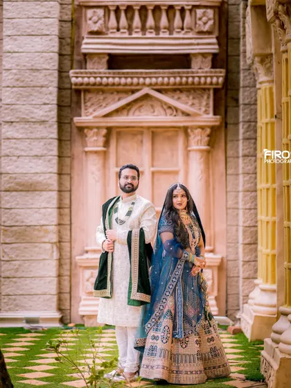 A grand, full-length portrait of a couple in front of an ornate building. Their royal blue and white outfits exude elegance and sophistication.