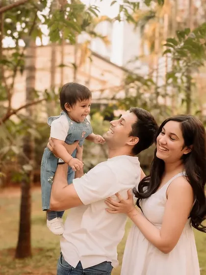 A classic portrait of a father holding his son, with mom looking on, framed by the lovely trees.