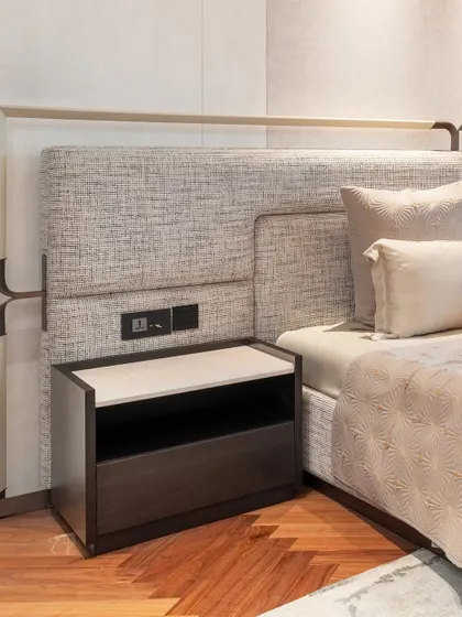 A close-up of a bespoke headboard with textured fabric and integrated bronze-finish metal details. The custom nightstand is designed to fit perfectly, demonstrating our commitment to creating seamless and thoughtful bedroom furniture.