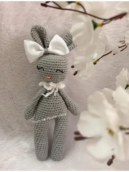 An elegant and sleepy-eyed bunny doll, this amigurumi is made in a chic grey yarn and finished with a large white satin bow.