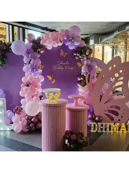A sophisticated butterfly-themed setup in a restaurant, using a large purple backdrop, organic balloon garland, and a giant butterfly wing prop for photos.