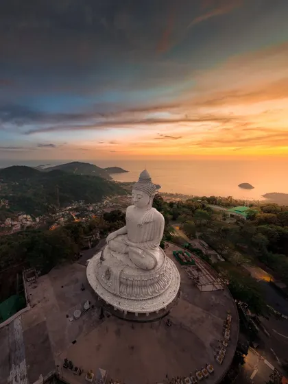 A wide panoramic shot of the Big Buddha statue overlooking the coastline of Phuket at sunset. The view from here is absolutely breathtaking.