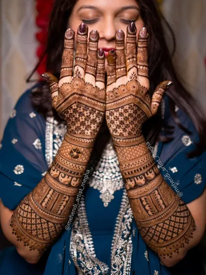 A classic pose where the bride shows off her full back-of-hand mehendi. The intricate geometric and traditional patterns are on full display.
