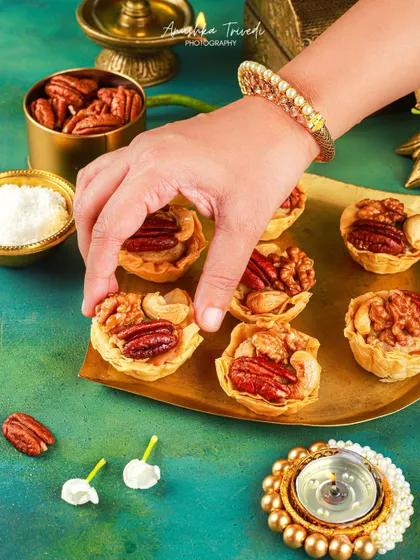 A hand with a traditional bangle picking up a mini nut tart, adding a human and festive element to the shot.