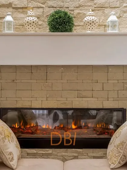 A close-up of a cozy fireplace with a stone-clad wall, creating a warm and rustic focal point in the living room. The mantelpiece is simply decorated, adding to the room's comfortable and inviting feel.