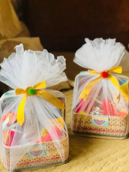 Two festive Rakhi hampers wrapped in white tulle with yellow ribbons, perfect for celebrating with family.