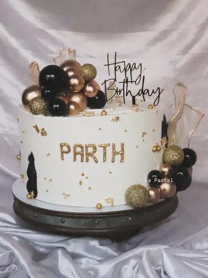 A bold and glamorous birthday cake in black, white, and gold. The balloon-like spheres and gold leaf make it a real showstopper.