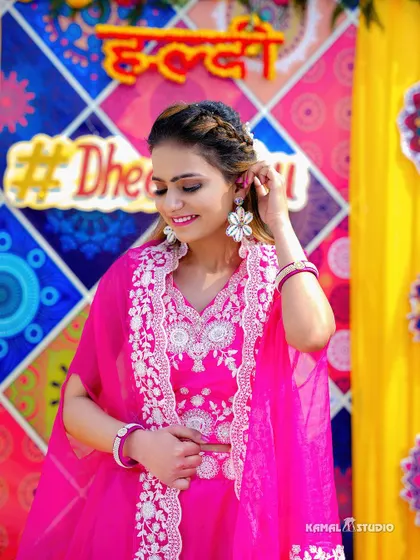A lovely portrait of the bride in her pink Haldi outfit, smiling against the colorful backdrop.