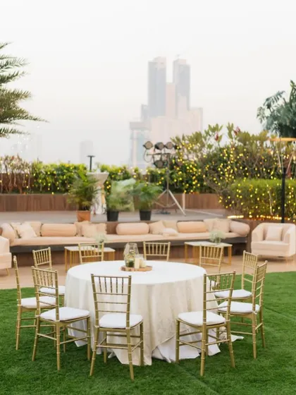 An outdoor reception setup with a mix of lounge seating and round tables, overlooking the city skyline.