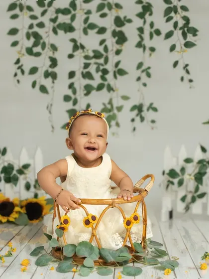 A 7-month-old baby girl beams with a huge smile, sitting in a basket surrounded by sunflowers. This setup is perfect for capturing the bright and cheerful personality of a sitter.