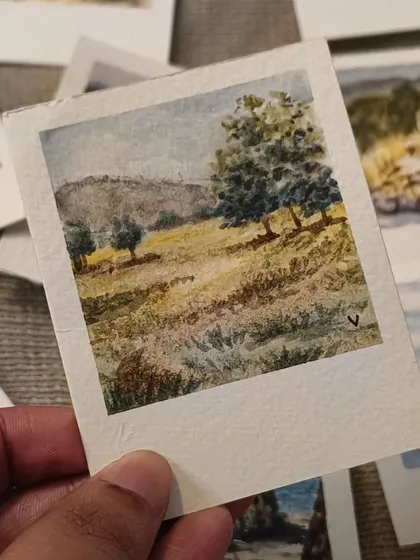 This watercolor Polaroid depicts a rolling, sunlit hill with scattered trees. The use of light and shadow gives this tiny landscape a sense of depth and warmth.