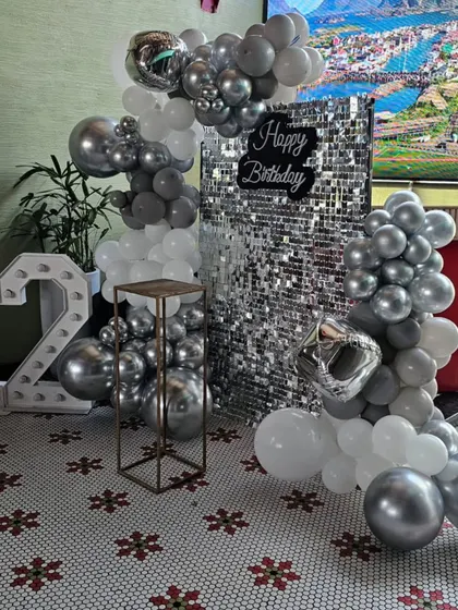 A chic and modern 12th birthday party setup with a silver and white theme, featuring a sequin backdrop and a metallic balloon garland.
