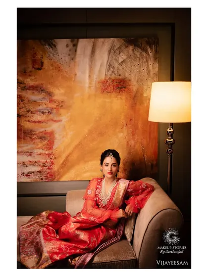 A wide shot of Krishna, showcasing her complete look against an artistic backdrop. The makeup stands out, enhancing her features and complementing the vibrant red of her outfit.