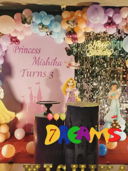 A Disney Princess party for a third birthday. This decoration features a silver shimmer wall, pastel balloon garland, and cutouts of popular princesses like Snow White, Rapunzel, Jasmine, and Ariel.