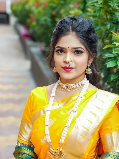 An elegant outdoor portrait of a bride in a vibrant yellow saree, showcasing her pearl necklace and traditional Maharashtrian look.