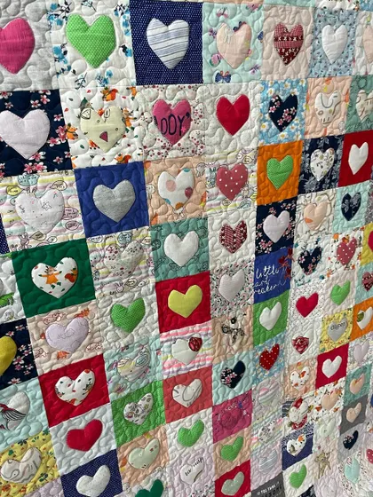 A detailed view of the heart appliqués, showcasing the variety of fabrics from the baby clothes used in this memory quilt.