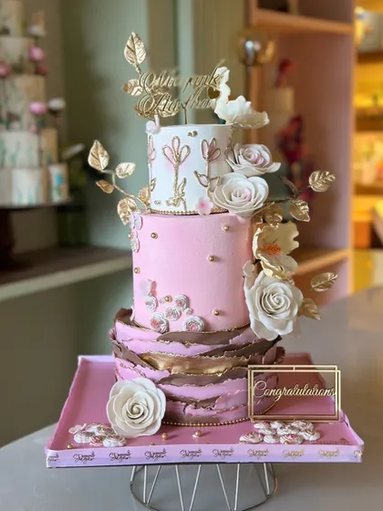 From behind the scenes to the final look, this three-tiered cake in pink and gold is a labor of love. It features a textured bottom tier, hand-painted floral details, and delicate sugar flowers.
