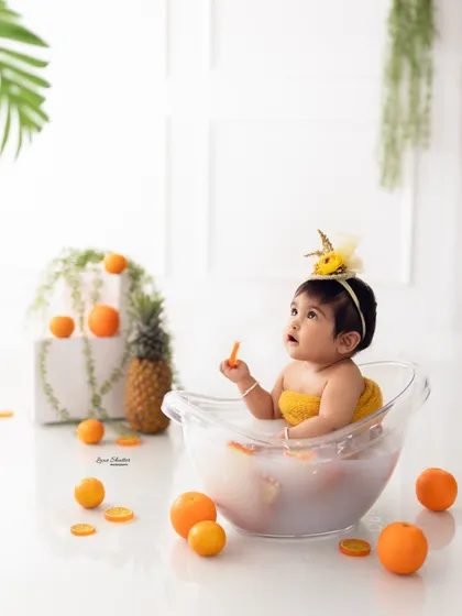 A nine-month-old baby girl enjoying her citrus-themed milk bath. The yellow headband and surrounding fruits create a cohesive and cheerful look.