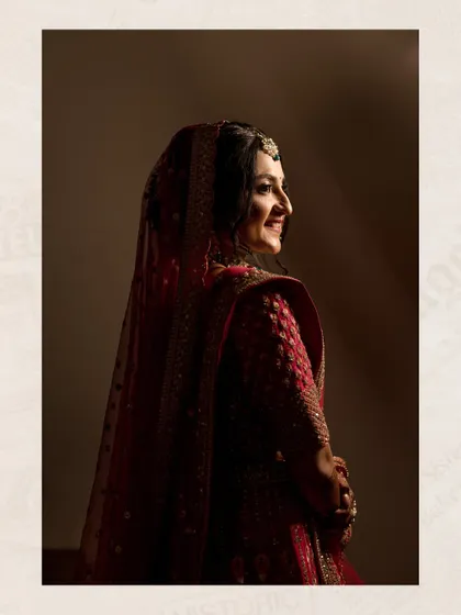 A beautiful bridal portrait using soft, dramatic lighting to highlight the bride's happy expression and her stunning red lehenga.