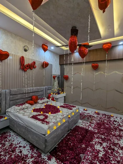 A romantic room surprise featuring red heart-shaped balloons, a 'LOVE' foil balloon, and the bed decorated with rose petals spelling out 'I ❤️ U'.