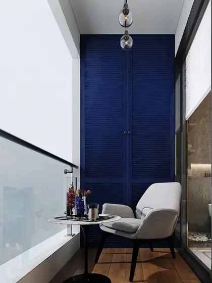 A small balcony transformed into a private coffee spot. The design features a comfortable chair, a small table, and a bold blue accent wall with louvered storage cabinets.